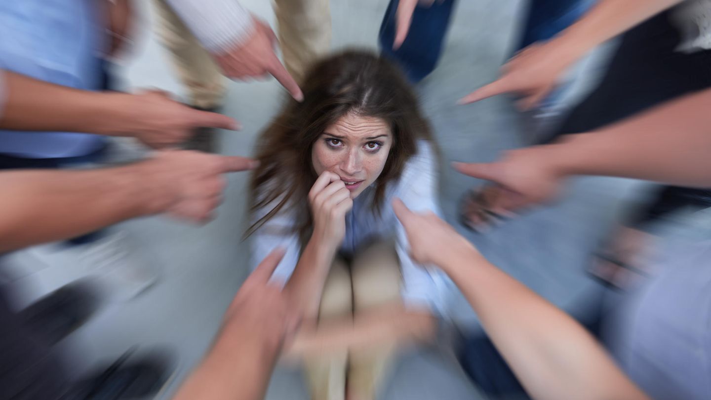 Eine Frau sitzt auf dem Boden, während viele Leute mit dem Finger auf sie zeigen.
