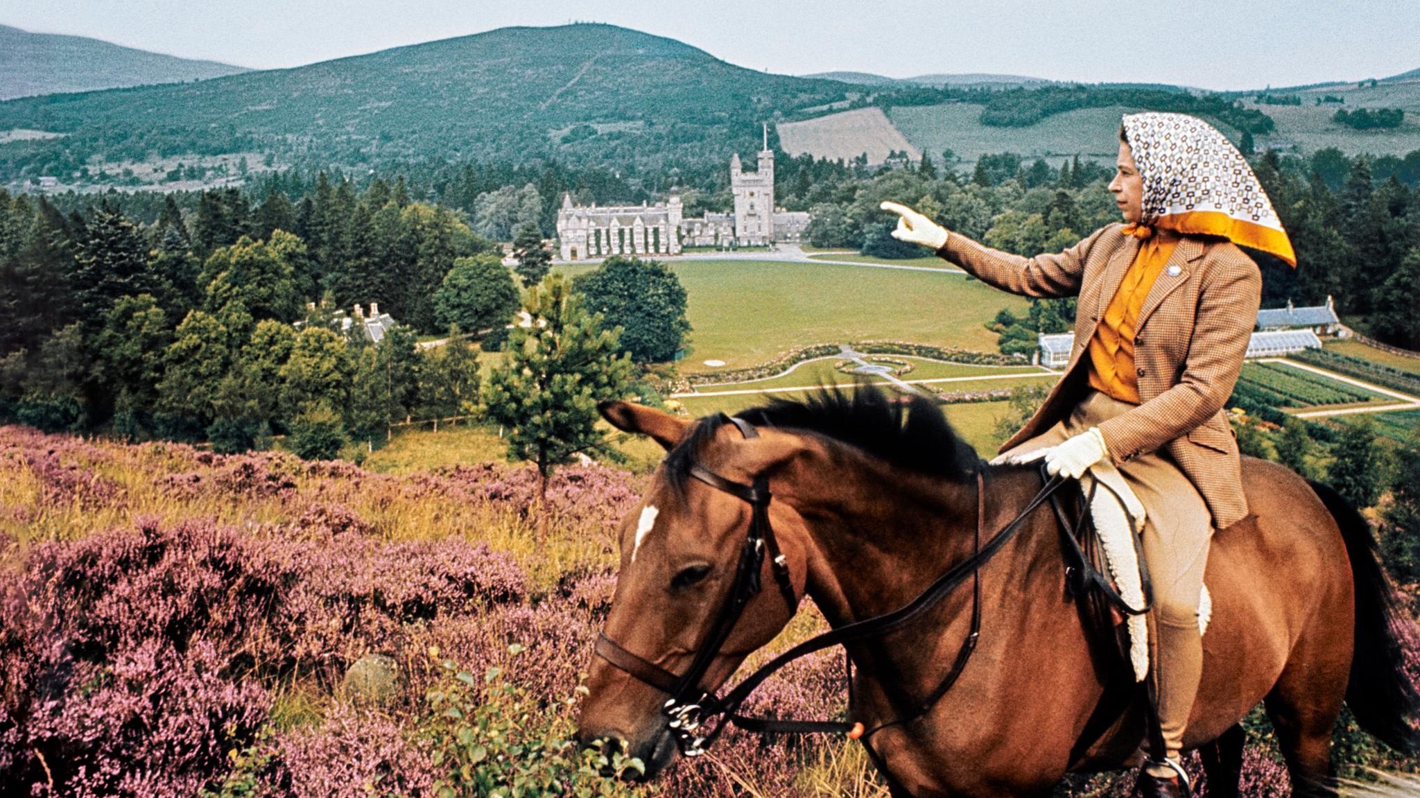 Die Queen, auf dem Rücken eines Pferdes, deutet auf Balmoral Castel in der Ferne