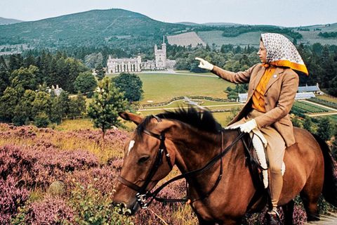 Die Queen, auf dem Rücken eines Pferdes, deutet auf Balmoral Castel in der Ferne