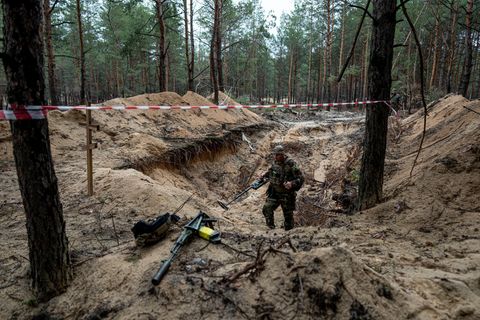 Ein ukrainischer Soldat inspiziert mit einem Metalldetektor ein Massengrab