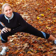 Laufen im Herbst: Eine Läuferin stretcht sich auf verlaubtem Boden