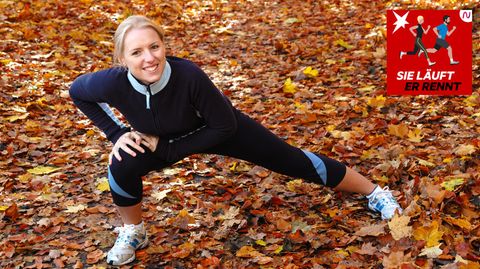 Laufen im Herbst: Eine Läuferin stretcht sich auf verlaubtem Boden
