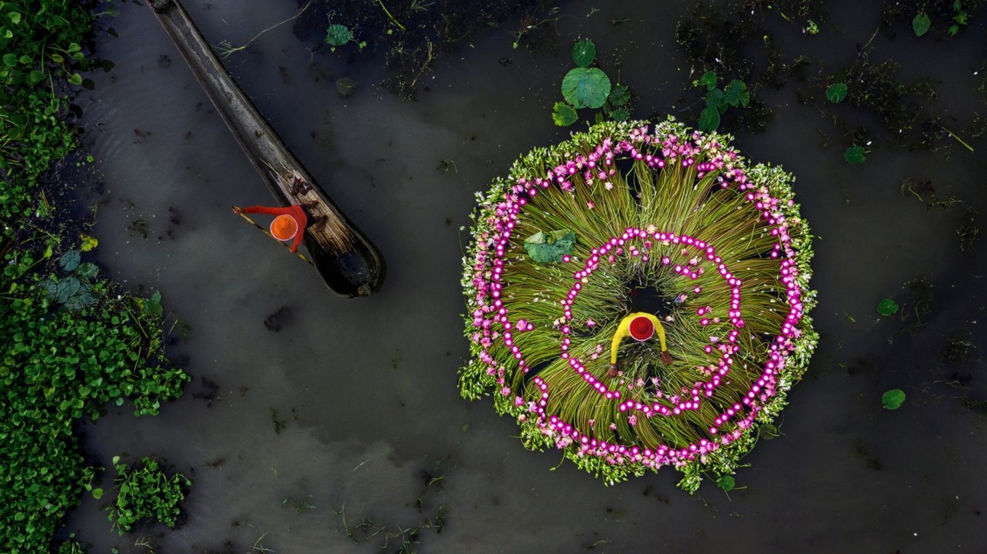 Zwei Arbeiter sind mit ihren bunten Hüten und Kleidern zu sehen inmitten von Seerosen zu sehen