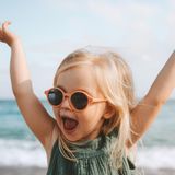 Ein kleines Mädchen hebt lachend ihre Arme in die Höhe.