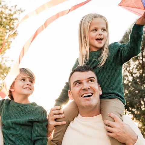 Zwei Männer spielen mit ihren zwei Kindern auf den Arm mit einem Drachen.