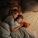 Eine Frau liegt mit ihrer Tochter kuschelnd im Bett.