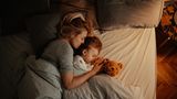 Eine Frau liegt mit ihrer Tochter kuschelnd im Bett.