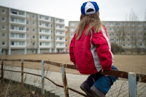 Ein Kind sitzt alleine im Innenhof eines Hochhausblocks