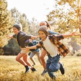Vier Kinder rennen gemeinsam durch einen herbstlichen Wald.