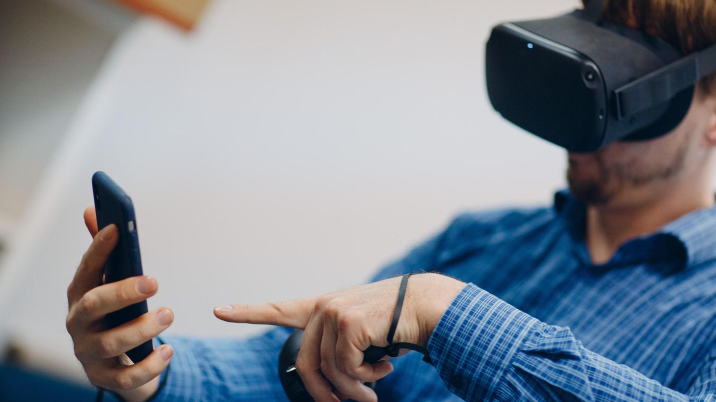 Hologramm-Telefonie: Ein Mann mit einer VR-Brille hält sein Handy in der Hand