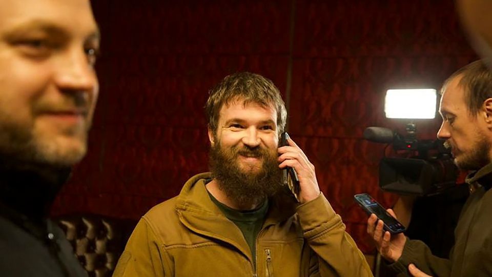 Prisoner Exchange Russia Ukraine A white man with a full beard and a military green sweater is smiling and talking on a mobile phone