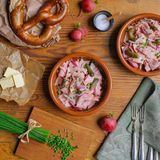 Bayerischer Wiesn Wurstsalat   Der Wurstsalat ist in Bayern ein typisches Gericht für den Biergarten.      Zutaten für 2 Personen  Vorbereitungszeit 15 Minuten  Zubereitungszeit 10 Minuten      100 ml Weißweinessig  3-4 Prisen Salz  4 Prisen Pfeffer  1 EL Zucker  1 TL mittelscharfer Senf  3 kleine, rote Zwiebeln  300 g Leberkäse (Neuburger) dünne Scheiben, 0,9 auf der Aufschnittmaschine  150 g Cornichons aus dem Glas  4 EL Sonnenblumenöl  1/2 Bund Schnittlauch      Beilagen:  2-4 frische Brezen  1 Bund Radieserl  80 g Butter      Zubereiten:  Essig in einer Schüssel mit Salz, Pfeffer, Zucker und Senf verrühren.  Die Zwiebeln halbieren und schälen.  Entweder dünne, feine Zwiebelstreifen oder feine Würfel schneiden und zum Essig geben.  Die Leberkäse-Scheiben exakt übereinander legen und zuerst 2,5 cm breite Streifen, dann 2,5 cm breite Rauten schneiden.  Die Leberkäse-Rauten auf dem Schneidebrett auseinander zupfen und dann in die Marinade legen.  Die Cornichons auf ein Sieb gießen, abtropfen lassen, anschließend der Länge nach halbieren oder in Scheiben schneiden.  Die Cornichons zum Leberkäse geben und gut vermischen. Den Salat mindestens 20 Minuten marinieren lassen.  Kurz vor dem Servieren nochmals abschmecken, nach Geschmack mit Öl ergänzen und anrichten.  Fein geschnittene Schnittlauchröllchen auf den Wurstsalat streuen und mit Brezen, Butter und Radieschen servieren.         Tipp von Koch Thomas Sixt:  Die Reihenfolge der Zubereitung ist für diesen Salat wichtig. Die rohen Zwiebeln sind, eingelegt in Essigmarinade länger haltbar. Den Salat können Sie im Kühlschrank gut einen Tag durchziehen lassen. Schnittlauch gebe ich stets frisch auf den angerichteten Salat, das Aroma ist so einfach besser.