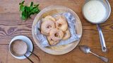 Wiesn-Apfelkiacherl mit falscher Vanille-Sauce  Die Apelkiacherl backen wir in Bayern traditionell im Bierteig. Aufgeblasen und knusprig muss der Teig nach dem Ausbacken sein. Damit es heute schneller geht, gibt es eine falsche Vanillesauce. Schließlich geht Oktoberfest-Küche auch mal schnell.  Zutaten für 4 Personen  Vorbereitungszeit 20 Minuten  Zubereitungszeit 20 Minuten      Falsche Vanille-Sauce:  4 Becher Vanillepudding  1 EL Cointreau      Backteig:  2 kalte Eier Größe M  1 Prise Salz  150 ml Münchner Helles  150 g Mehl  1 TL Puderzucker  1/2 TL Backpulver      Äpfel:  6 Stück Äpfel (Elstar)  300-500 g Rapsöl      Dekoration:  100 g Zucker  1 TL Zimt  1 Bund frische Minze      Zubereiten:  Den Vanillepudding in einer Schüssel mit dem Cointreau verrühren und bis zum Servieren kalt stellen.  Die Eier trennen, die Eiweisse mit einer Prise Salz zu Eischnee schlagen und kalt stellen.  Die Eigelbe leicht anschlagen. Das Bier dazu geben und das Mehl frisch gesiebt mit dem Puderzucker und dem Backpulver einrühren.  Die Äpfel schälen, mit einem Apfelausstecher das Kernhaus entfernen.  Das Rapsöl in einem großen Topf oder in der Fritteuse auf 160-170°C erhitzen.  Den Eischnee zum Bierteig geben und luftig unterheben. Die Teig-Masse soll luftig und gut verbunden sein.  Die Äpfel in 1 cm dicke Scheiben schneiden.  Die Apfelscheiben mit einer langen Pinzette in den Teig tauchen, gut abtropfen lassen, dann im heißen Öl beidseitig knusprig 3-4 Minuten ausbacken.  Die Apfelscheiben aus dem heißen Fett entnehmen und auf einem Küchenkrepp kurz abtropfen lassen.      Anrichten:  Die Apfelringe im Zimtzucker wenden und auf Teller legen.  Mit der Vanille-Sauce servieren und frische Minze dazu reichen.      Tipp von Koch Thomas Sixt:  Der Bierteig lässt sich ebenso mit trockenem Weißwein zubereiten. Der Teig ist auch ausgezeichnet zum Ausbacken von Gemüse geeignet.