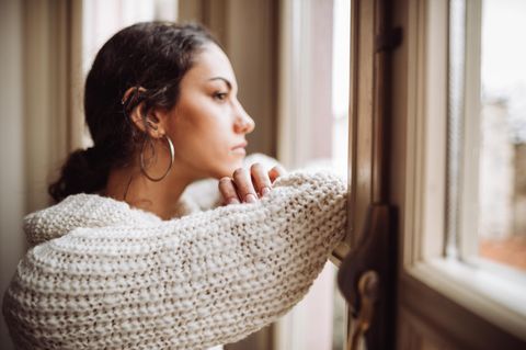 Eine junge Frau schaut besorgt aus dem Fenster.
