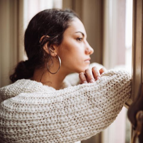 Eine junge Frau schaut besorgt aus dem Fenster.