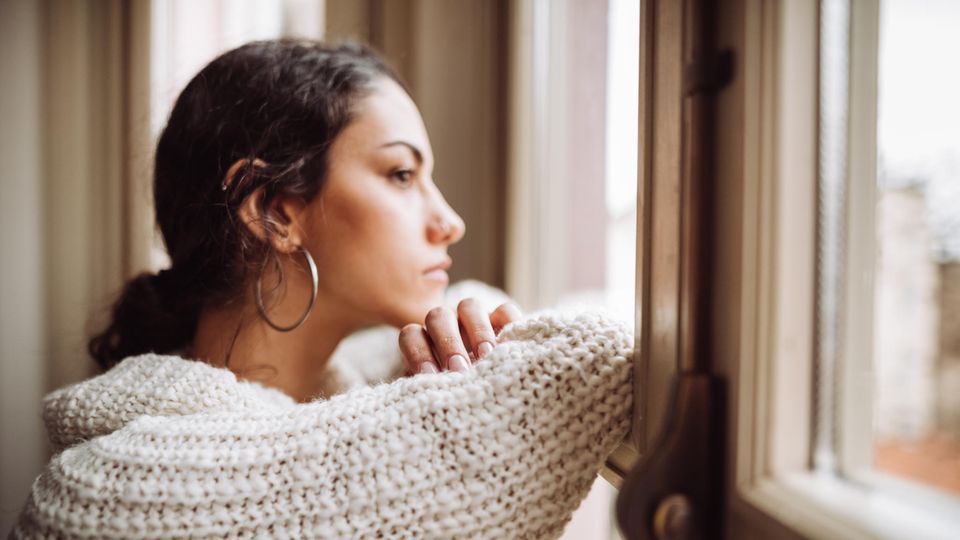 Eine junge Frau schaut besorgt aus dem Fenster.