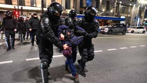 Zwei Polizisten in blauen Uniformen und mit schwarzen Helmen drücken den Oberkörper eines Festgenommenen nach unten