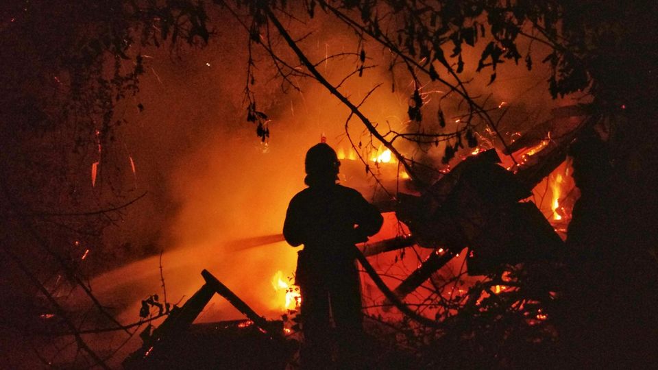 Ein Feuerwehrmann vor einem brennenden Haus