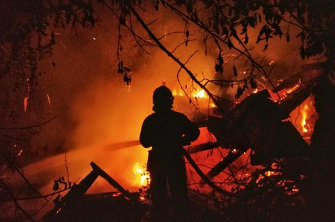 Ein Feuerwehrmann vor einem brennenden Haus