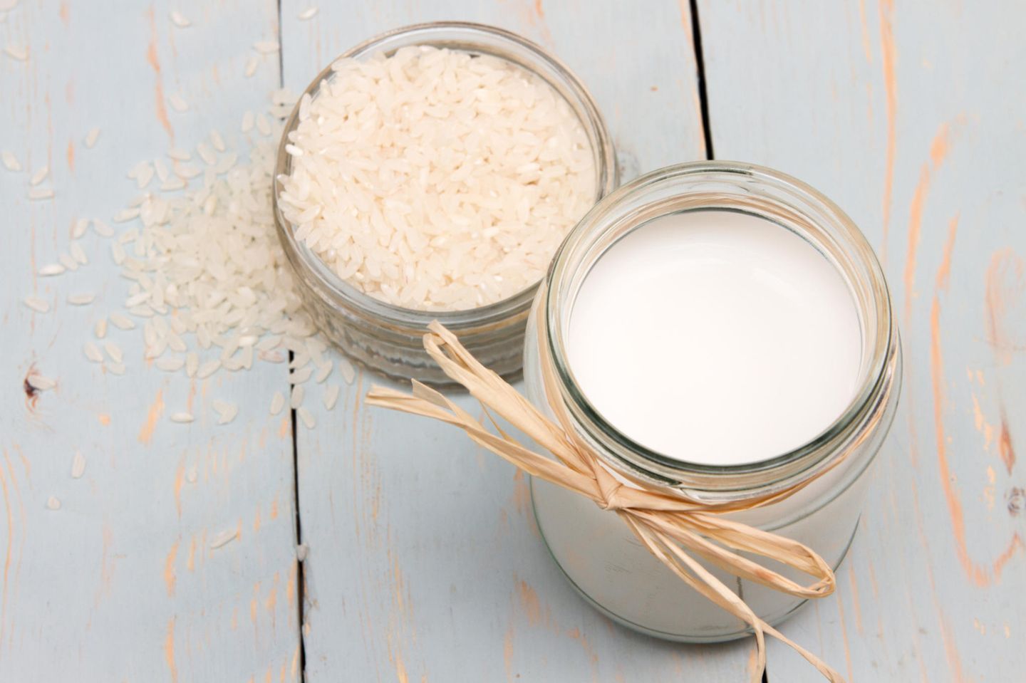 Eine kleine Schüssel mit rohem Reis und daneben ein Glas mit Reismilch auf Holzuntergrund