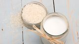 Eine kleine Schüssel mit rohem Reis und daneben ein Glas mit Reismilch auf Holzuntergrund