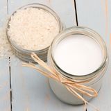 Eine kleine Schüssel mit rohem Reis und daneben ein Glas mit Reismilch auf Holzuntergrund