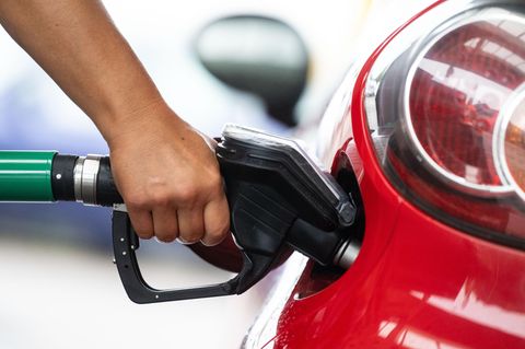 Eine Hand hält an einer Tankstelle ein Zapfventil in den Tank eines roten Autos