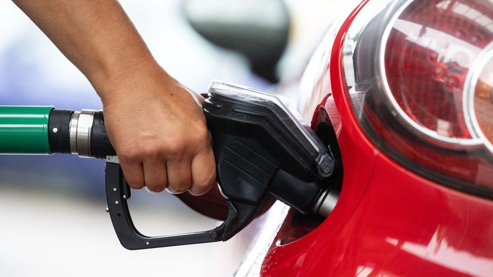 Eine Hand hält an einer Tankstelle ein Zapfventil in den Tank eines roten Autos
