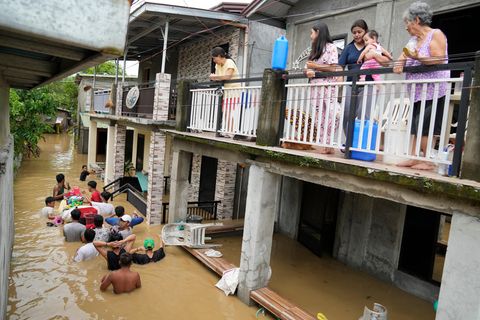 Philippinen: Anwohner halten sich auf der Terrasse ihres Hauses auf, während andere eine überschwemmte Straße passieren