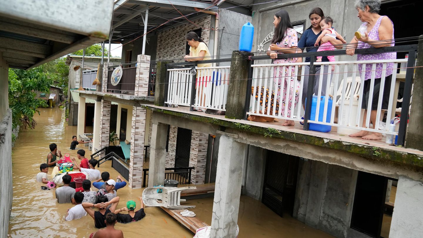 Philippinen: Anwohner halten sich auf der Terrasse ihres Hauses auf, während andere eine überschwemmte Straße passieren
