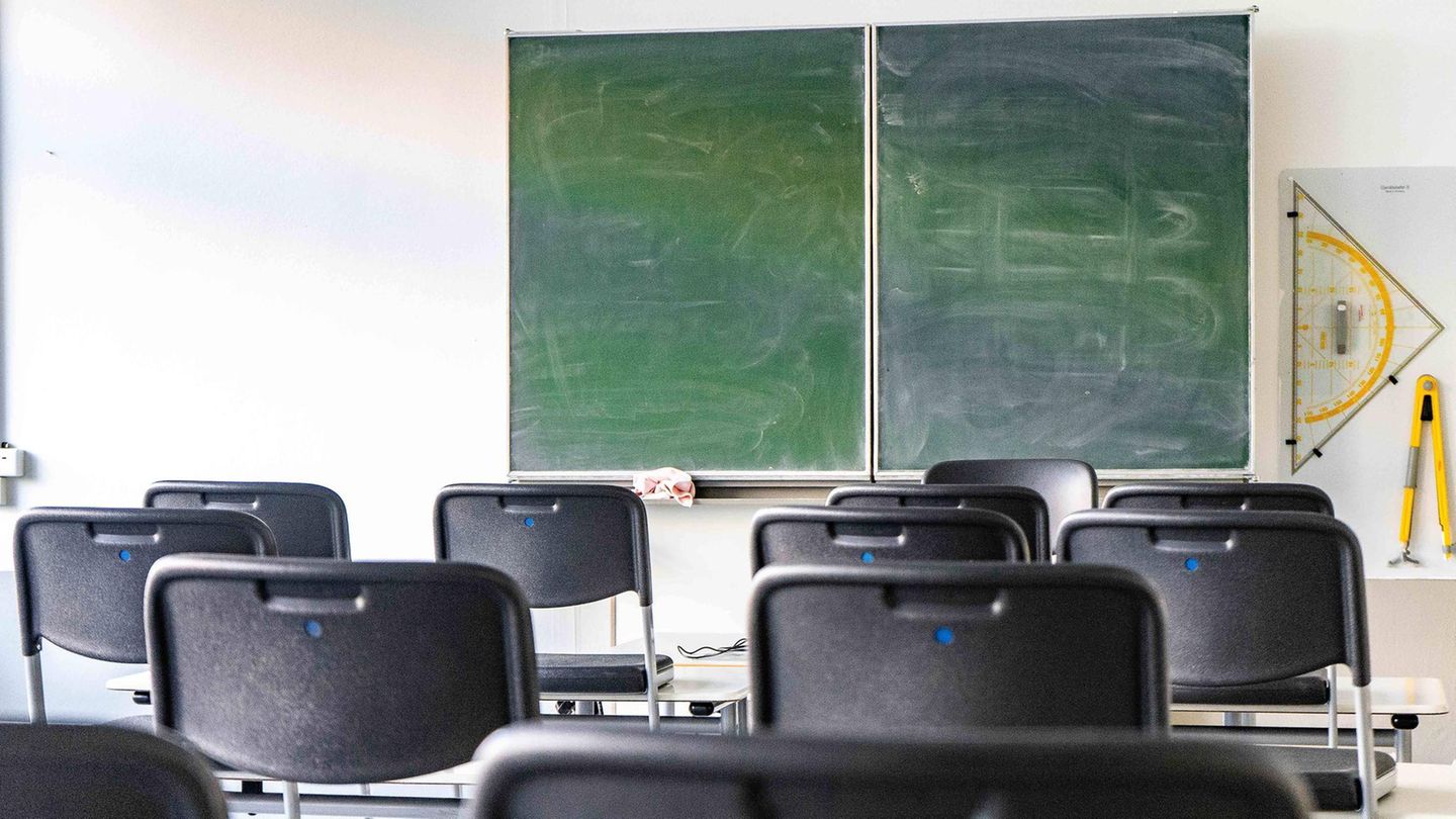Graue Stühle stehen in einem leeren Klassenzimmer vor einer Tafel