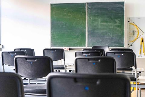 Graue Stühle stehen in einem leeren Klassenzimmer vor einer Tafel