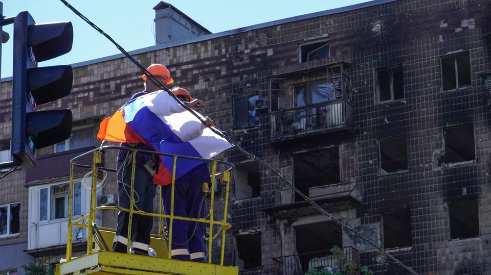 Arbeiter befestigen eine russische Flagge uber einer Straße in Mariupol
