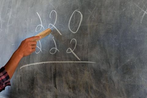 Eine Hand hält einen kurzen Zeigestock in der Hand und zeigt damit auf eine Schultafel