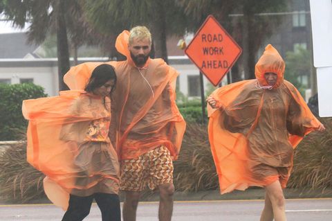 Ein Mann und zwei Frauen gehen in orangen Regencapes über eine Straße im US-Bundesstaat Florida