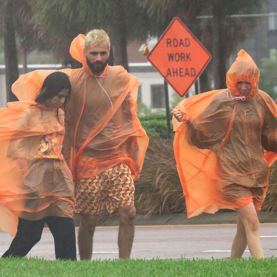 Ein Mann und zwei Frauen gehen in orangen Regencapes über eine Straße im US-Bundesstaat Florida