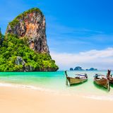 Drei Holzboote liegen an einem Strand mit türkisblauem Wasser.