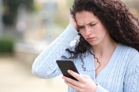Eine Frau blickt irritiert auf ihr Smartphone - Es kursiert eine neue Betrugsmasche per SMS