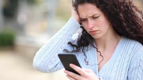 Eine Frau blickt irritiert auf ihr Smartphone - Es kursiert eine neue Betrugsmasche per SMS