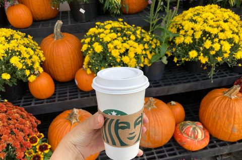 Frau hält Starbucks-Becher vor Kürbissen