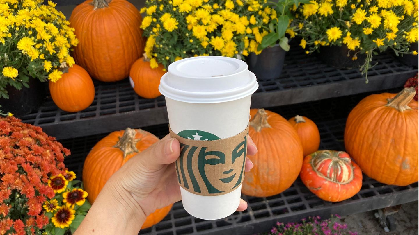 Frau hält Starbucks-Becher vor Kürbissen