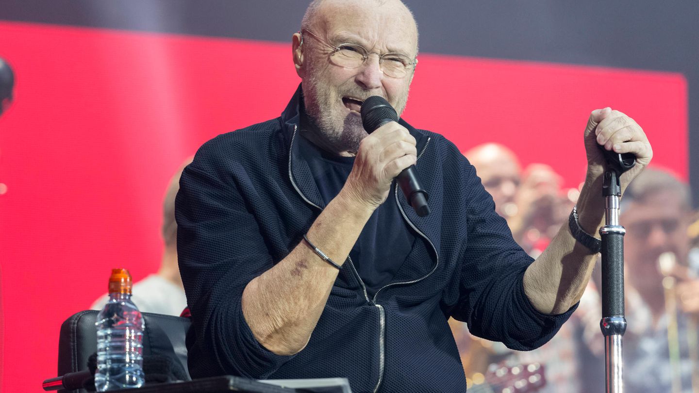 Phil Collins mit Mikrofon in der Hand bei einem Auftritt auf der Bühne