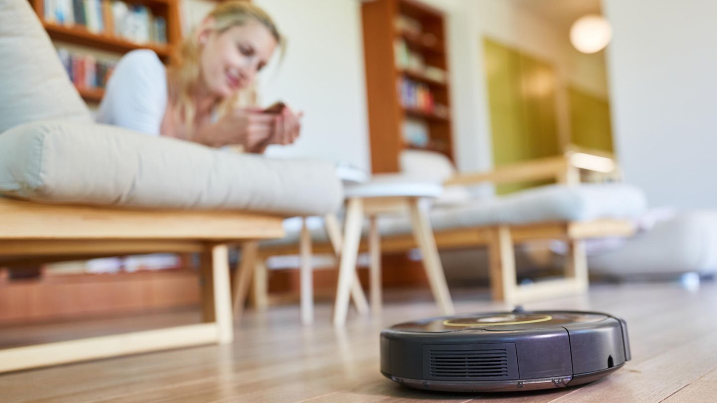 Eine Frau liegt auf dem Sofa, ein Saugroboter fährt vorbei. Ein IT-Experte ist besorgt.