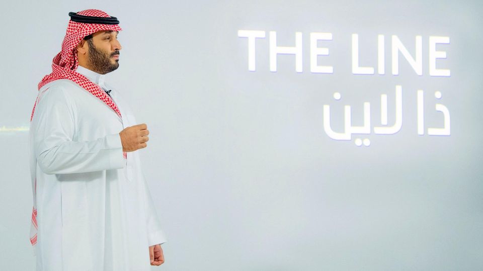 Der Kronprinz Saudi-Arabiens, Mohammed bin Salman, steht im Profil vor einer weißen Wand mit dem Schriftzug "The Line"