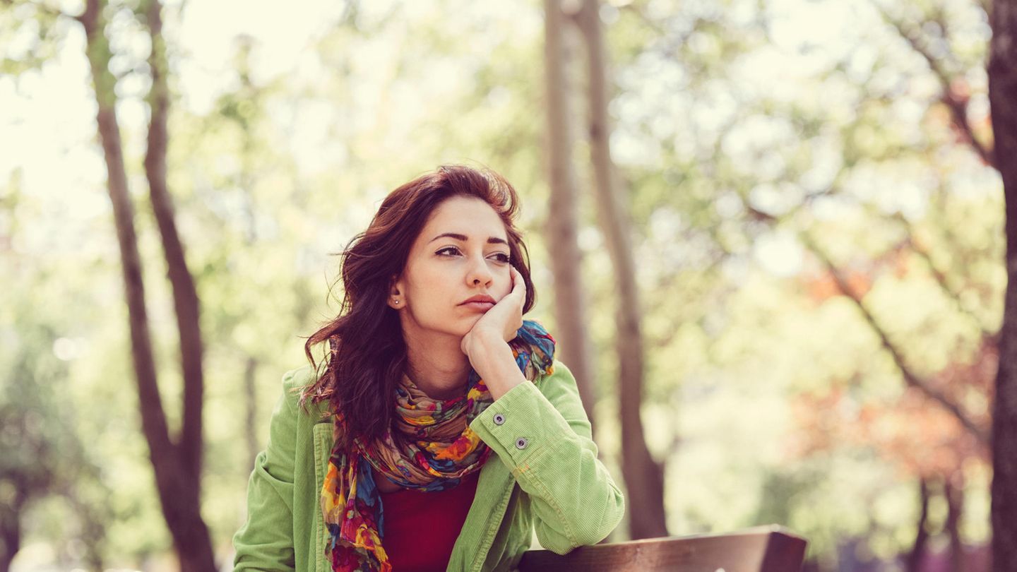 Eine Frau sitzt alleine auf einer Parkbank und guckt traurig in die Ferne.