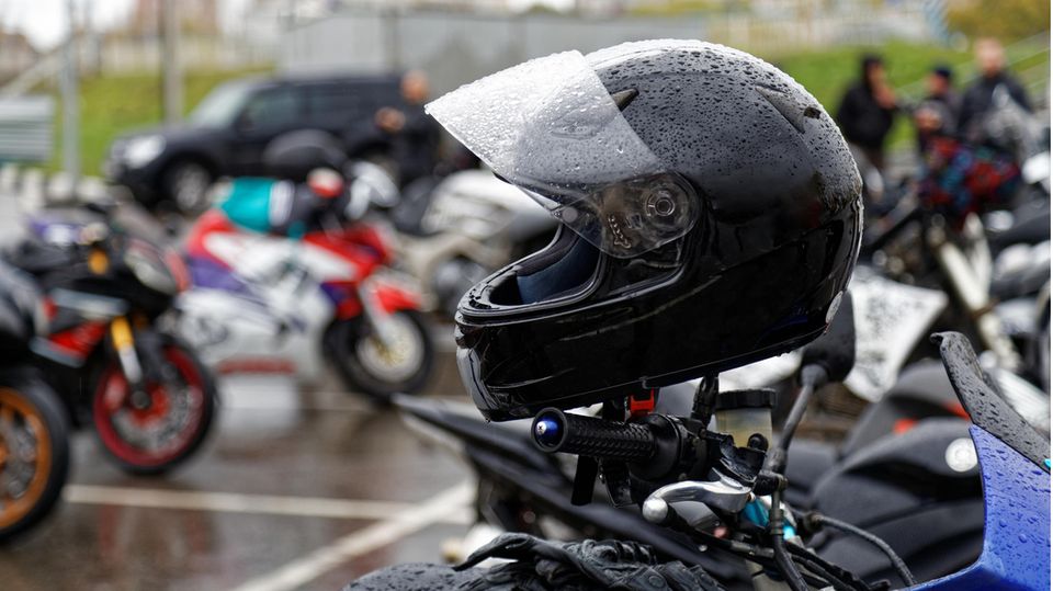 Motorradfahrer in voller Gangart und Helm mit Regenschirm im Regen