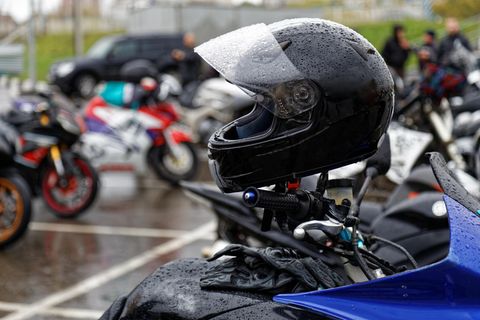 Motorradfahrer in voller Gangart und Helm mit Regenschirm im Regen