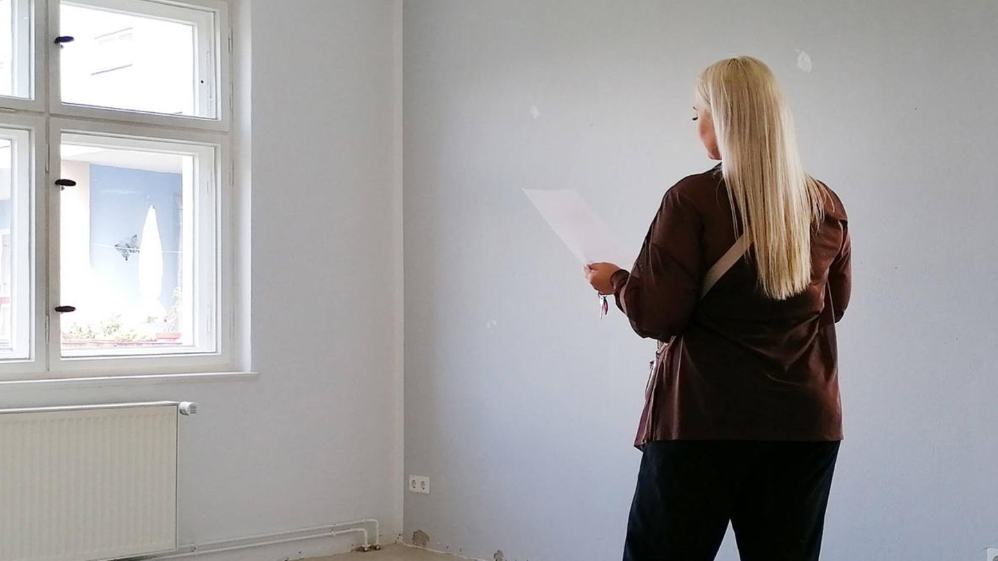 Eine Frau steht bei einer Wohnungsbesichtigung in einem leeren Raum und schaut auf ein Blatt