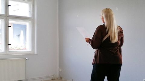 Eine Frau steht bei einer Wohnungsbesichtigung in einem leeren Raum und schaut auf ein Blatt