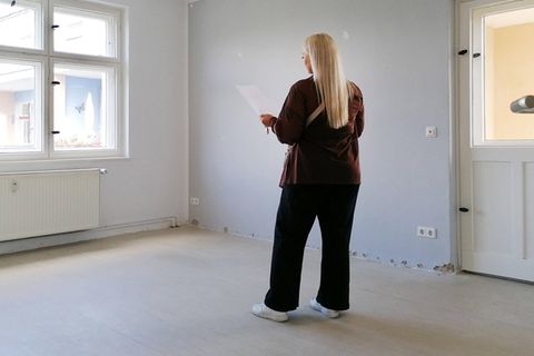 Eine Frau steht bei einer Wohnungsbesichtigung in einem leeren Raum und schaut auf ein Blatt